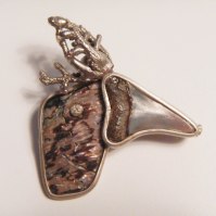 Brooch: a fragment of mother of pearl from New Zealand, a sharktooth from Perù and a piece of a broken brooch in silver from Los Arayanes wood in Argentina (the woods that inspired the setting for Walt Disney’s Bambi) are the elements that compose this head of an exotic bird. The piece is finished in silver, little diamand as a pupil . Spilla: Testa d'oca: frammento di madreperla neozelandese, un dente di squalo dal Perù e un ciuffetto di bacca argentato proveniente dal bosco argentino de Los Arayanes che ispirò Walt Disney per il bosco di Bambi, nasce la testa di upupa-renna! Spilla con rifiniture in argento, diamantino punto luce 0.01 KT come pupilla.